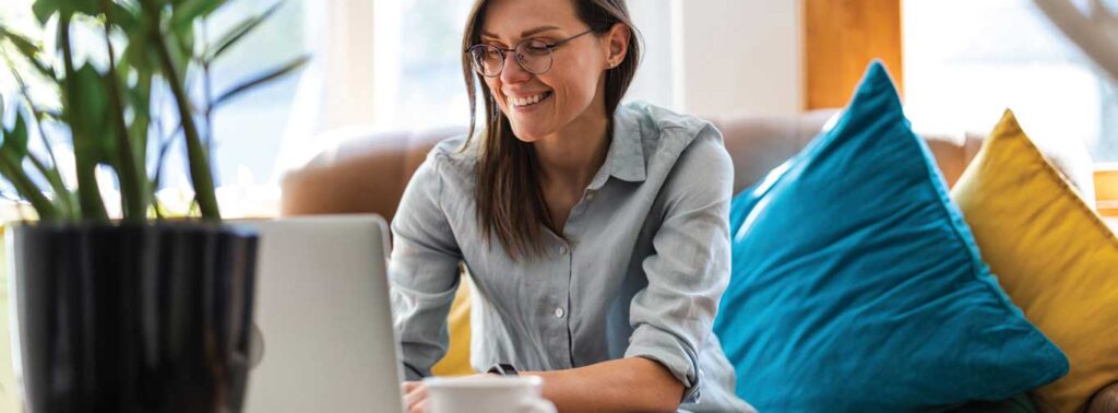 InMind Behavioral Health FAQs, woman sitting on a bright couch while typing on a laptop